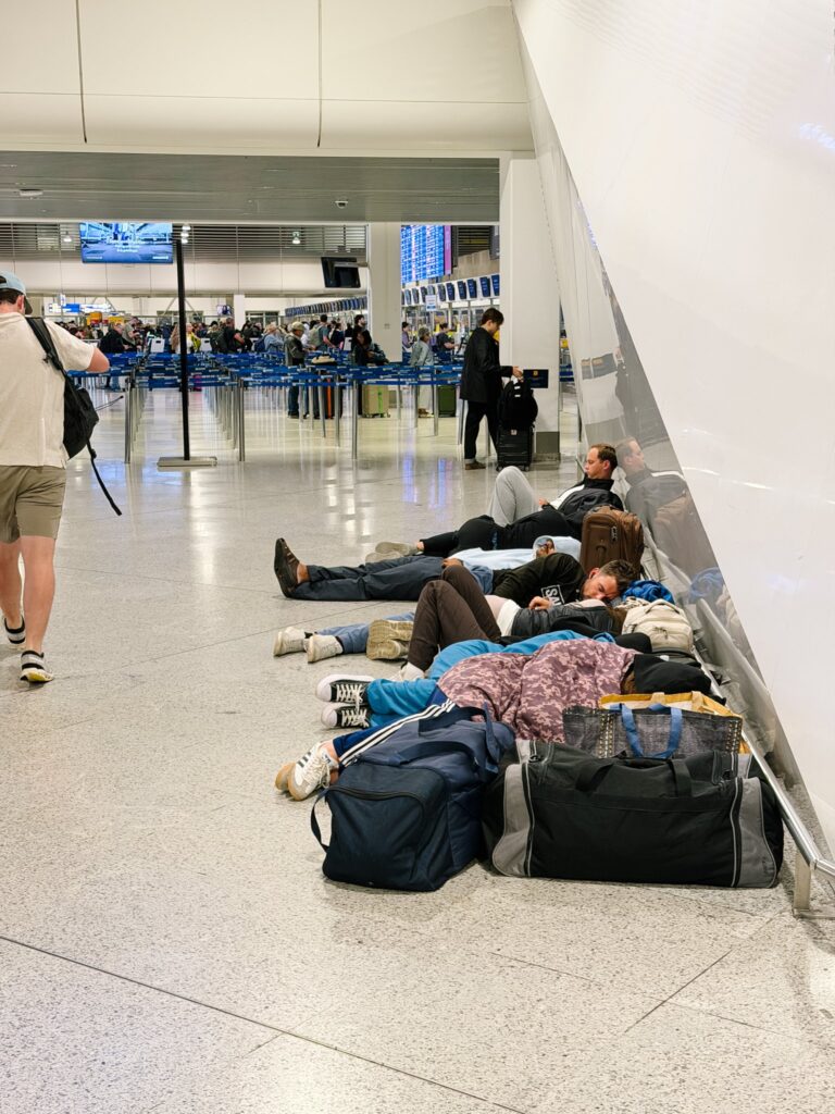 Travelers sleeping on the floor of an airport terminal next to their bags after missing their flights