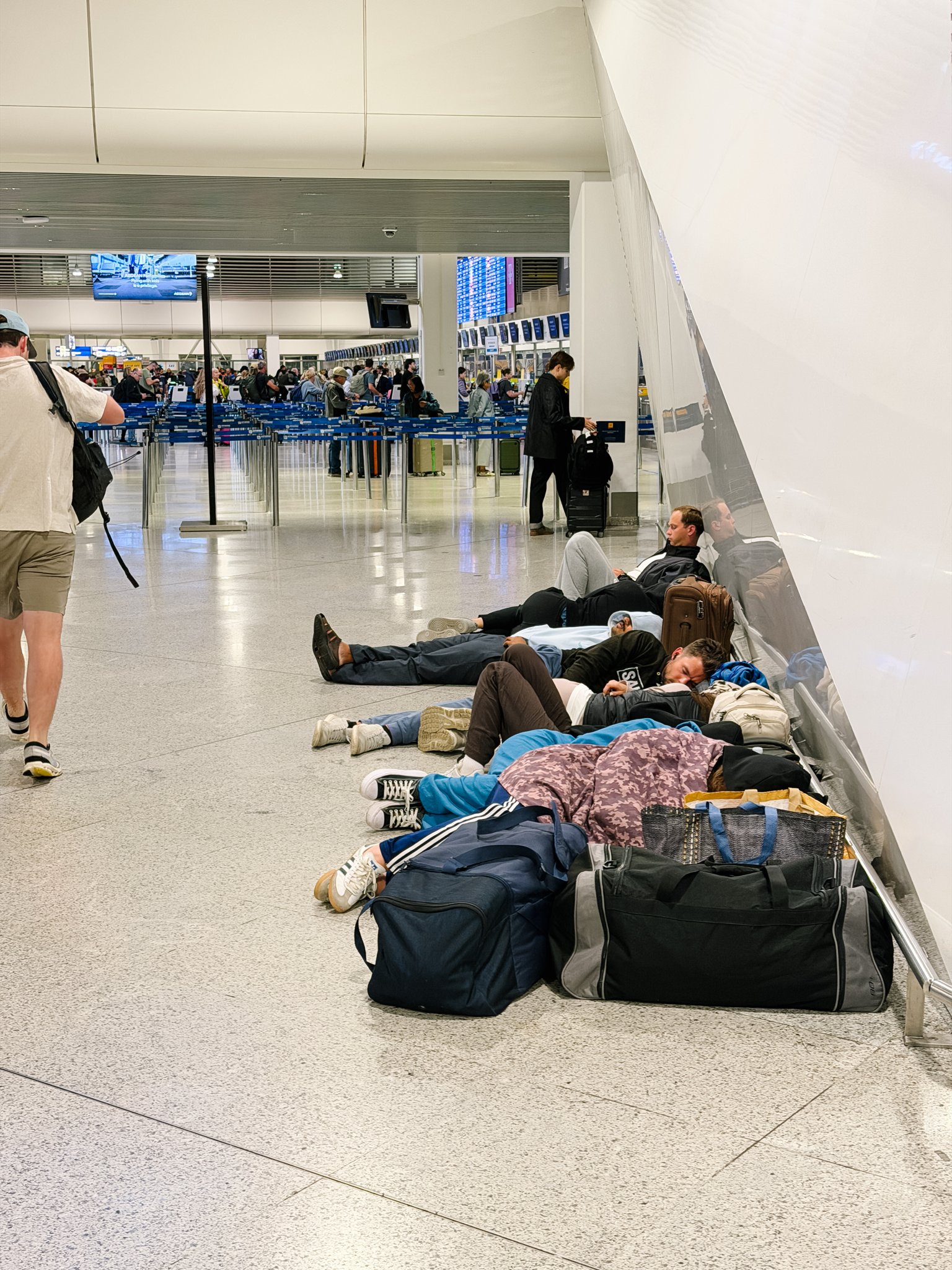 Travelers sleeping on the floor of an airport terminal next to their bags after missing their flights