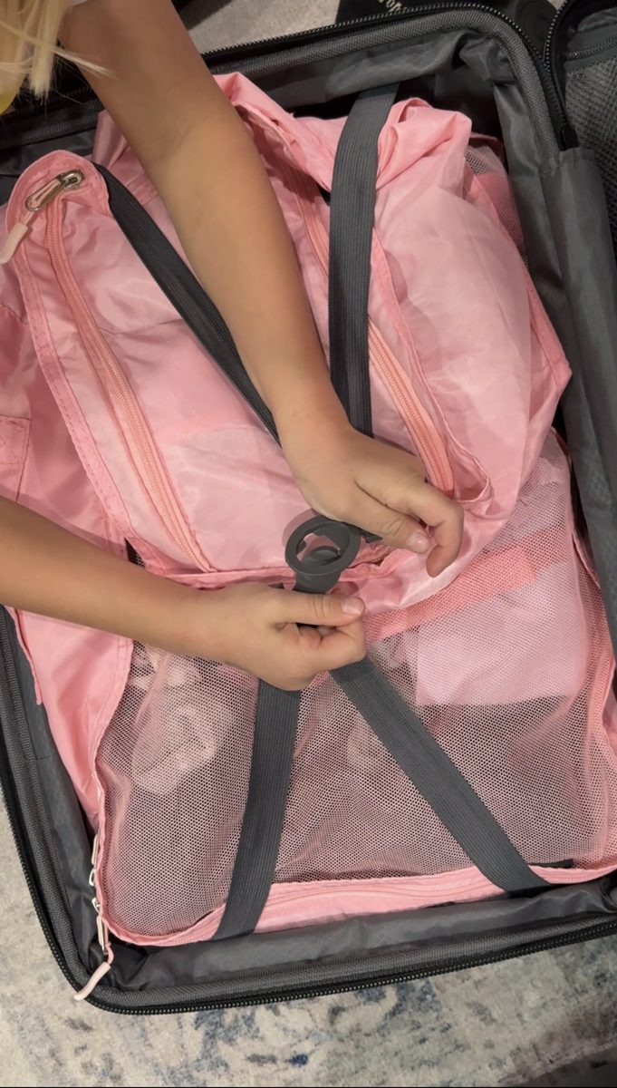 Child packing pink packing cubes into a suitcase