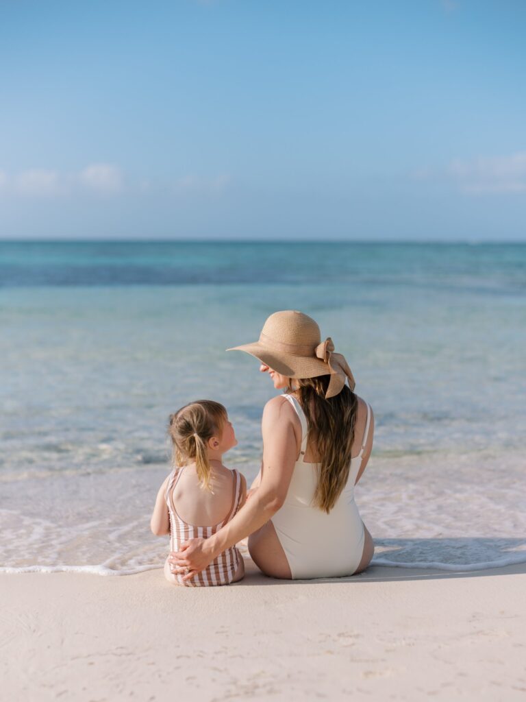 Mom and daughter sitting at the water’s edge on a white sand beach